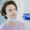 Une femme dans un établissement médical se fait tester le COVID-19 par écouvillonnage nasal, portant un masque et souriant.
