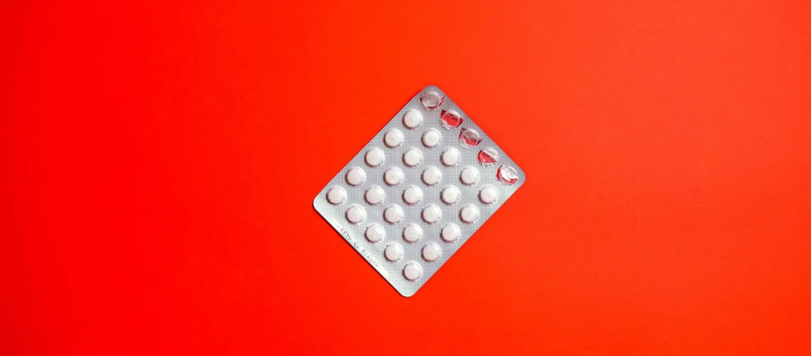 Gros plan d'une plaquette de pilules sur fond rouge uni symbolisant les soins de santé et les médicaments.